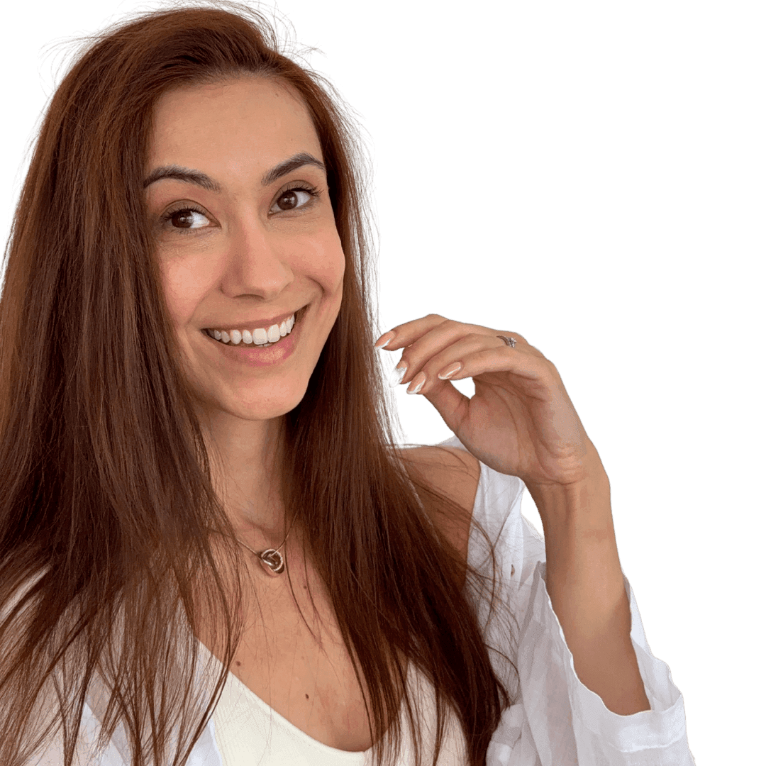 Smiling woman with long brown hair wearing a white top, touching her hair with one hand.